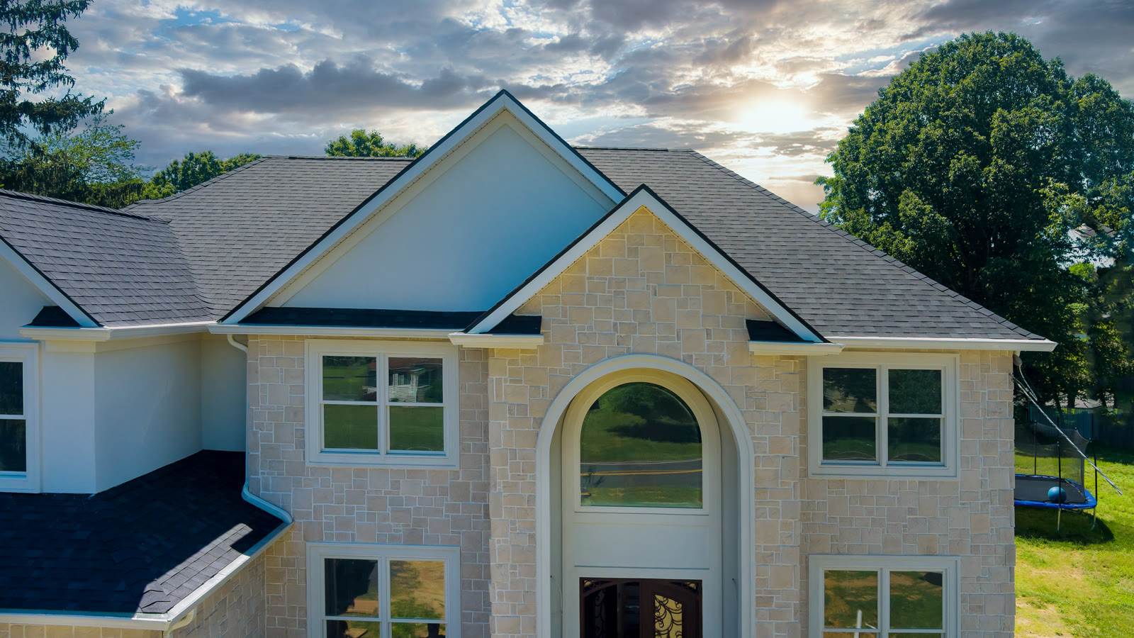 Modern stone-and-siding home with an asphalt-shingle roof at sunset