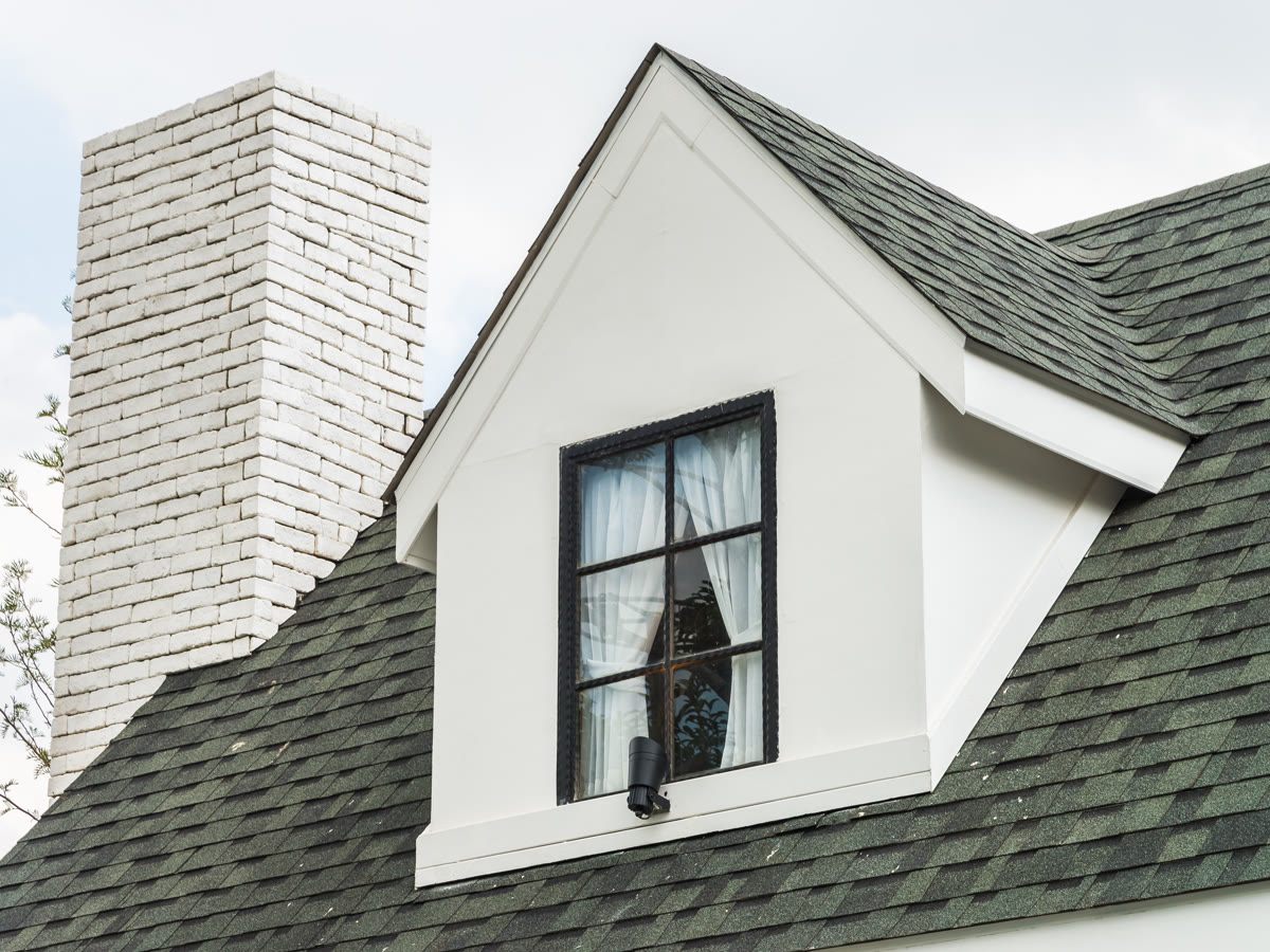 Asphalt-shingle roof around a white dormer and brick chimney